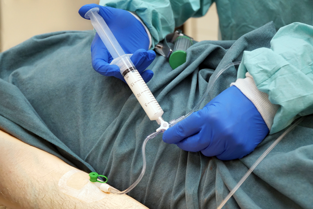 Médico anestesista aplicando sedativo intravenoso em paciente deitado na maca.